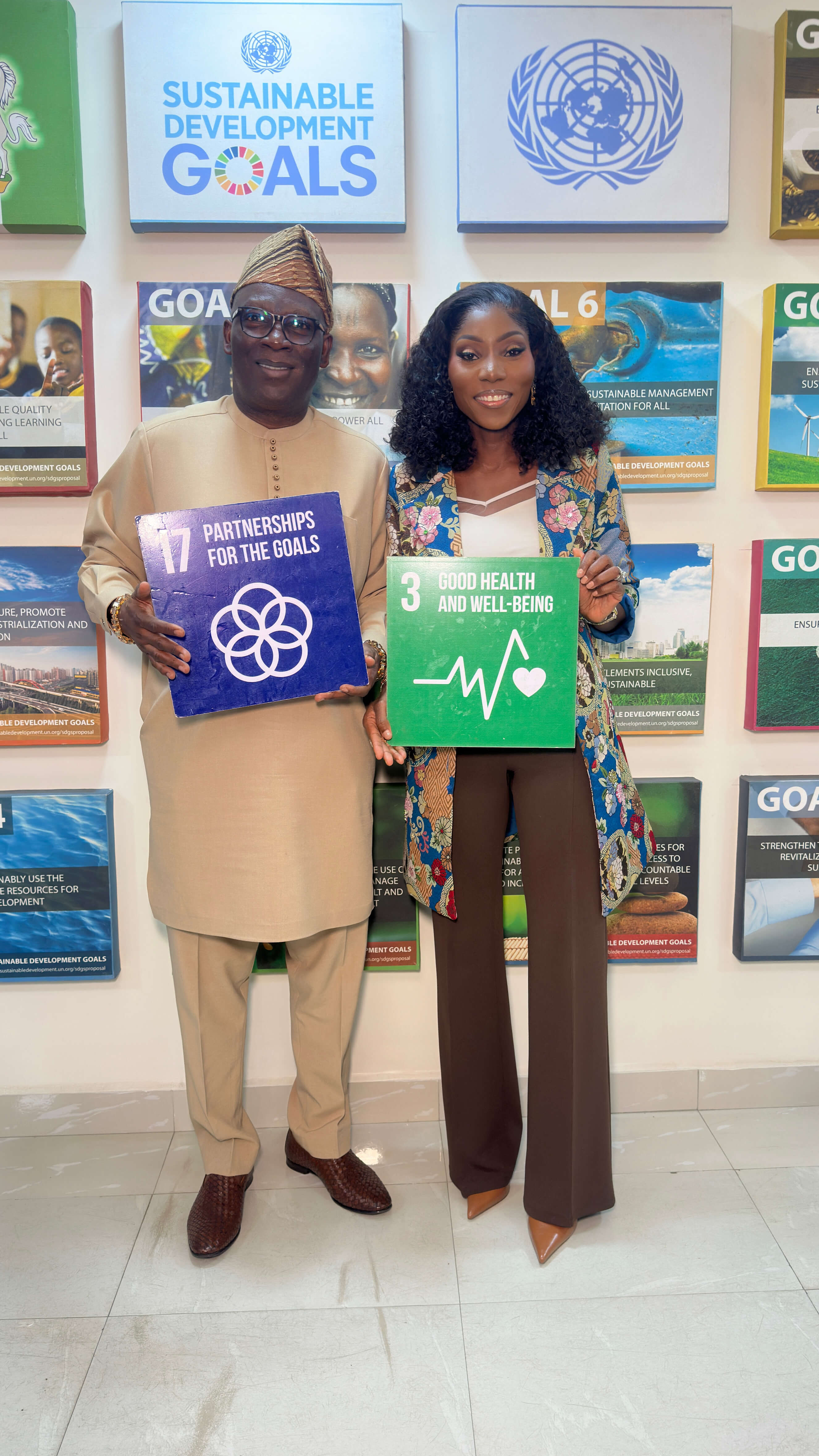 The same two people pointing to SDG Goal 3 on a wall display.