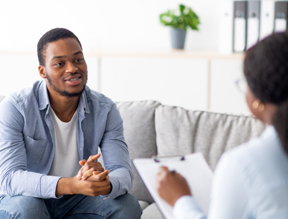 Effective psychotherapy. Young black guy talking to his psychologist, receiving professional help at mental health clinic. African American male patient sharing therapy results with counselor