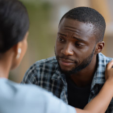 Compassionate black female therapist comforting distressed young man in clinic Emotional support theme 
