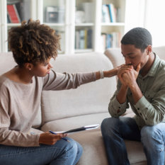 Young african woman psychologist consoling upset man 