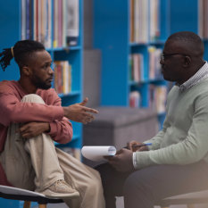 Side view portrait of black student talking to mental health therapist or guidance counselor in college library 