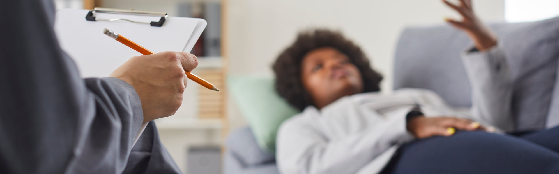 Woman visits professional therapist. Relaxed African American lady lying on sofa and talking about her problems with psychotherapist who is taking notes on paper. Therapy, psychotherapy concept