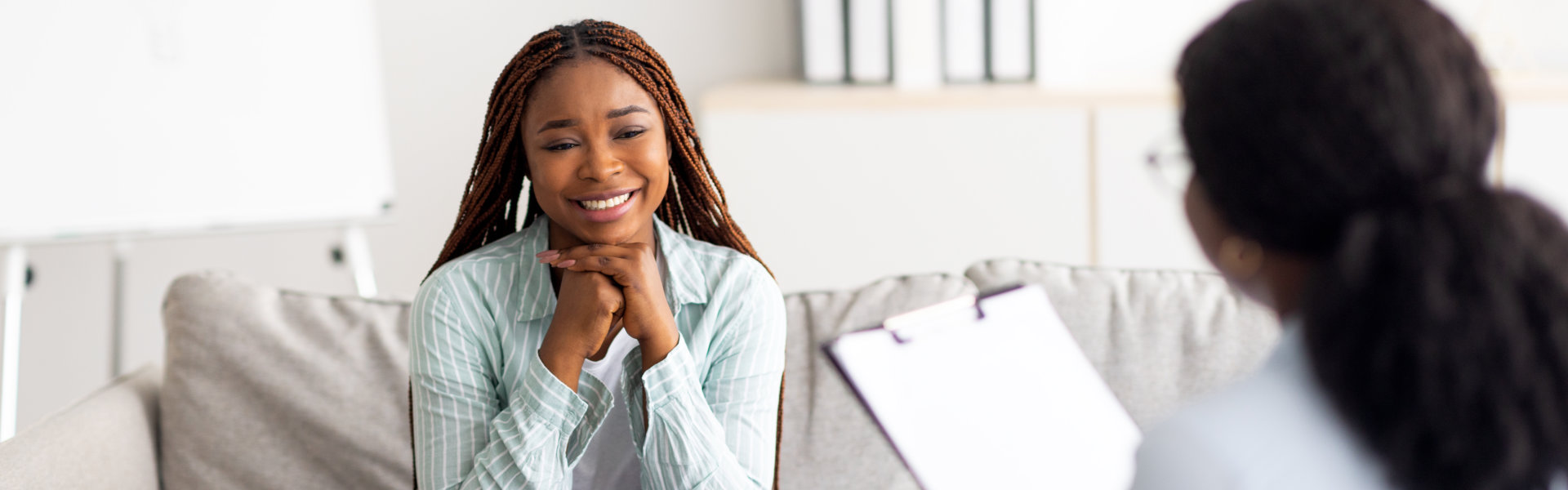 Successful psychotherapy. Millennial female client having session with psychologist, smiling, sitting on couch at clinic