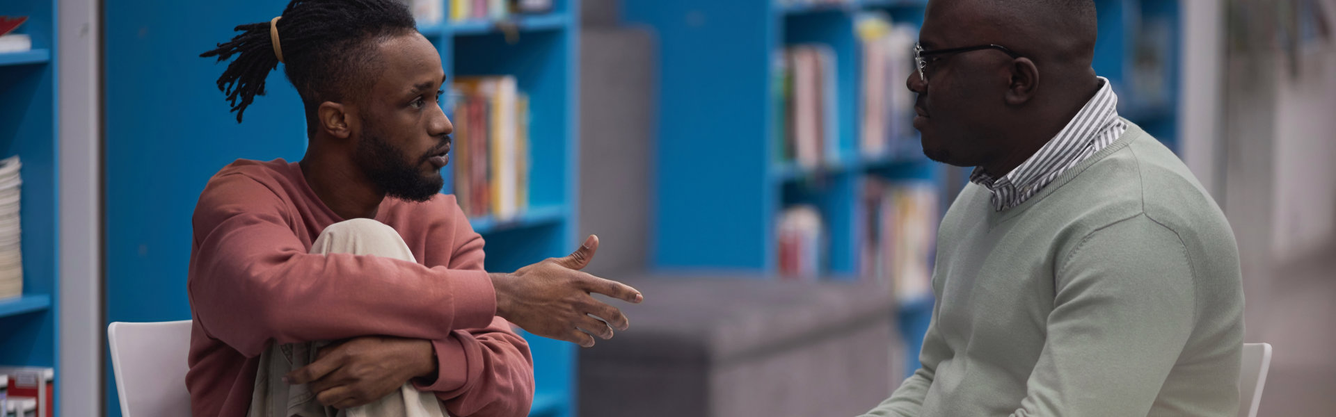 Side view portrait of black student talking to mental health therapist or guidance counselor in college library